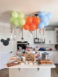 mickey mouse balloons are hanging from the ceiling above a kitchen island filled with food and snacks