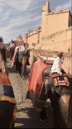 several people riding on the backs of elephants down a street in front of an old building