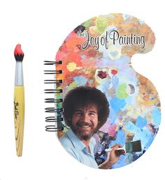 an artist's notebook with a pencil and photo of bob ross on it next to a brush