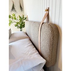 a bed with white pillows and a wooden headboard hanging on the wall next to a potted plant