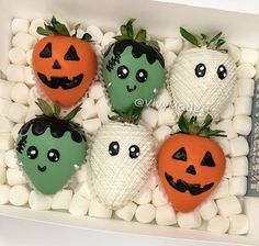 four decorated strawberries in a box with marshmallows and jack - o'- lantern faces