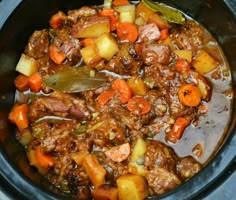 a crock pot filled with meat, potatoes and carrots