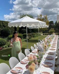 a woman standing next to a long table with plates and flowers on it in front of an umbrella