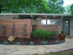 a modern home with wood fence and plants in the front yard, surrounded by stone pavers