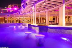 an indoor swimming pool at night with purple lights on the ceiling and steps leading up to it