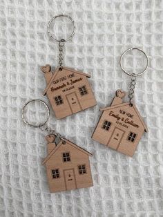 three wooden key chains with houses engraved on the front and back, sitting on a white blanket