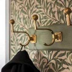 coat rack with hooks on wall next to green and white floral wallpaper, hanging from hooks