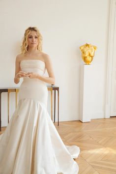 a woman in a white wedding dress standing next to a table with a vase on it