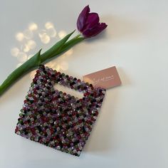 a purple flower sitting on top of a white table next to a bag with beads