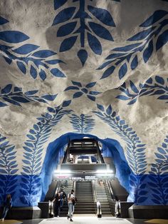 an escalator in a building with blue leaves painted on the ceiling