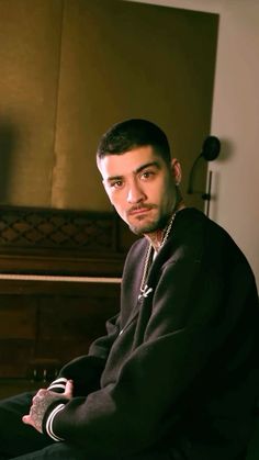 a man sitting in front of a piano wearing a black sweatshirt and silver chain around his neck