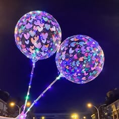 two balloons with hearts on them are lit up at night