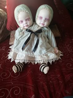 two dolls sitting on top of a bed next to each other