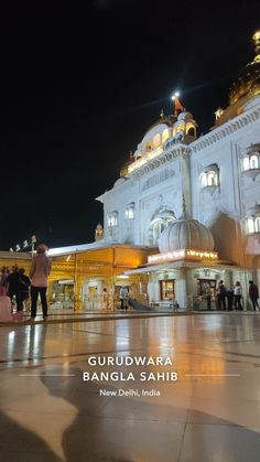 people standing in front of a large building at night with lights on the top floor