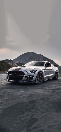 a silver sports car parked on top of a parking lot next to a mountain range