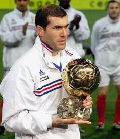 a man holding a soccer ball and trophy in front of other men on the field