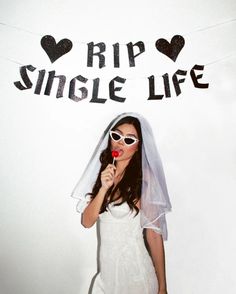 a woman wearing sunglasses and a veil holding a lollipop in front of a sign that says rip single life