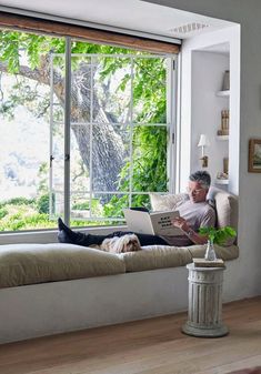 a man sitting on a window sill using a laptop computer while his dog lays next to him