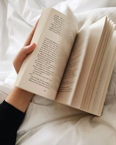 someone is reading a book in bed with their hand on top of the open book