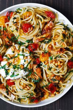 a white bowl filled with pasta and meat on top of a wooden table next to sliced lemons