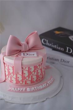 a birthday cake with a pink bow on top and a book in the back ground