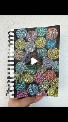 a hand holding up a spiral notebook with colorful balls on it