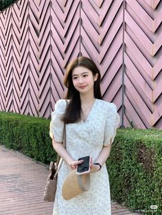 a woman standing in front of a pink wall holding a purse and cell phone with her hand