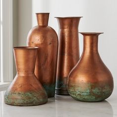 three copper vases sitting on top of a white counter