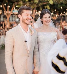 a bride and groom smile as they walk down the aisle at an outdoor wedding ceremony