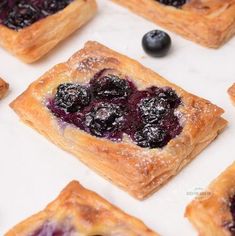 small pastries with blueberries and powdered sugar sit on a white counter top