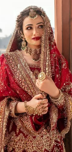 a woman in a red and gold bridal outfit with jewelry on her head, posing for the camera