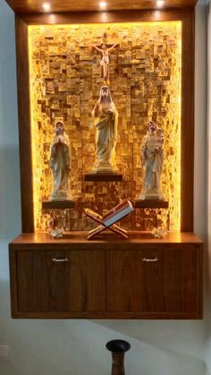 an illuminated shrine with three statues in the center and a cross above it on a wooden shelf