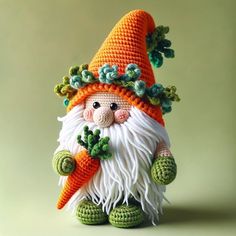 a crocheted gnome holding a carrot on top of a green surface with leaves