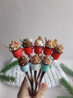 a hand is holding several small cupcakes with frosting on them and topped with christmas decorations