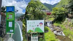 a green phone booth sitting on the side of a road next to a stream and bridge