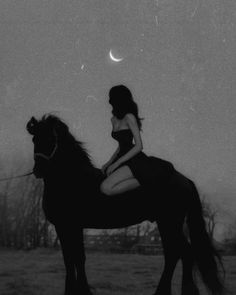 a woman riding on the back of a black horse next to a moon filled sky