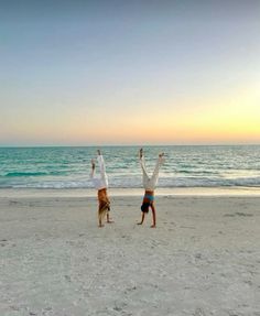 two people doing handstands on the beach at sunset