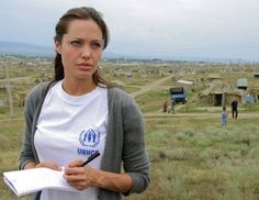 a woman holding a pen and paper in her hand while standing on a field with tents