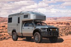 a truck with a camper attached to the back parked on top of a dirt field