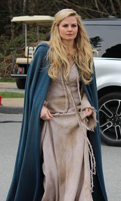 a woman in a long dress is walking down the street with a blue coat over her shoulders