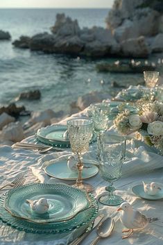 the table is set with white flowers and glassware for an elegant dinner by the ocean