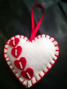 a red and white heart shaped ornament hanging on a black leather surface with a red ribbon