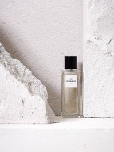 a bottle of perfume sitting on top of a white shelf next to a stone wall