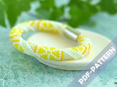 a yellow and white beaded bracelet sitting on top of a plate next to green leaves