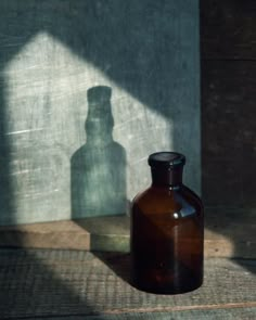 a brown glass bottle sitting on top of a wooden floor next to a shadow cast wall