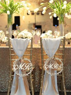 two tall vases filled with white flowers sit next to each other on top of a table