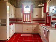 a kitchen with red tile flooring and white cupboards on the walls, windows, and cabinets