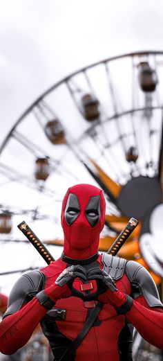 a man dressed as deadpool holding two baseball bats in front of a ferris wheel