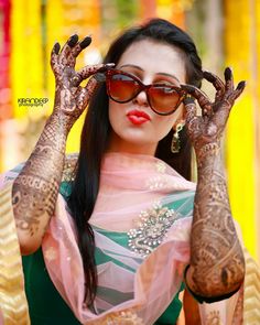 a woman with henna tattoos holding her hands up to her face and wearing sunglasses