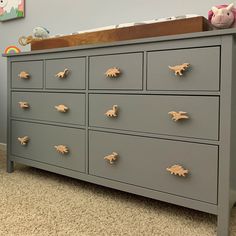 a gray dresser with dinosaur knobs on it's drawers in a child's bedroom